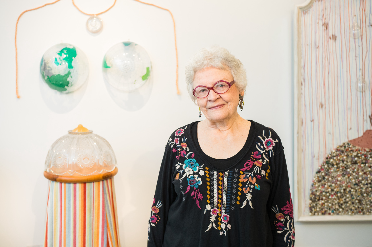 Portrait of Carol Cole Levin in her studio with her artwork (created under the name Carol Cole), left to right: Mother Earth (after Lee Lozano), 2008; The Grand Nanny, 2015; and When the Saint Goes Marching In, 1996. Photography by Carolyn de Berry, all images courtesy of the Weatherspoon Art Museum, UNC Greensboro.