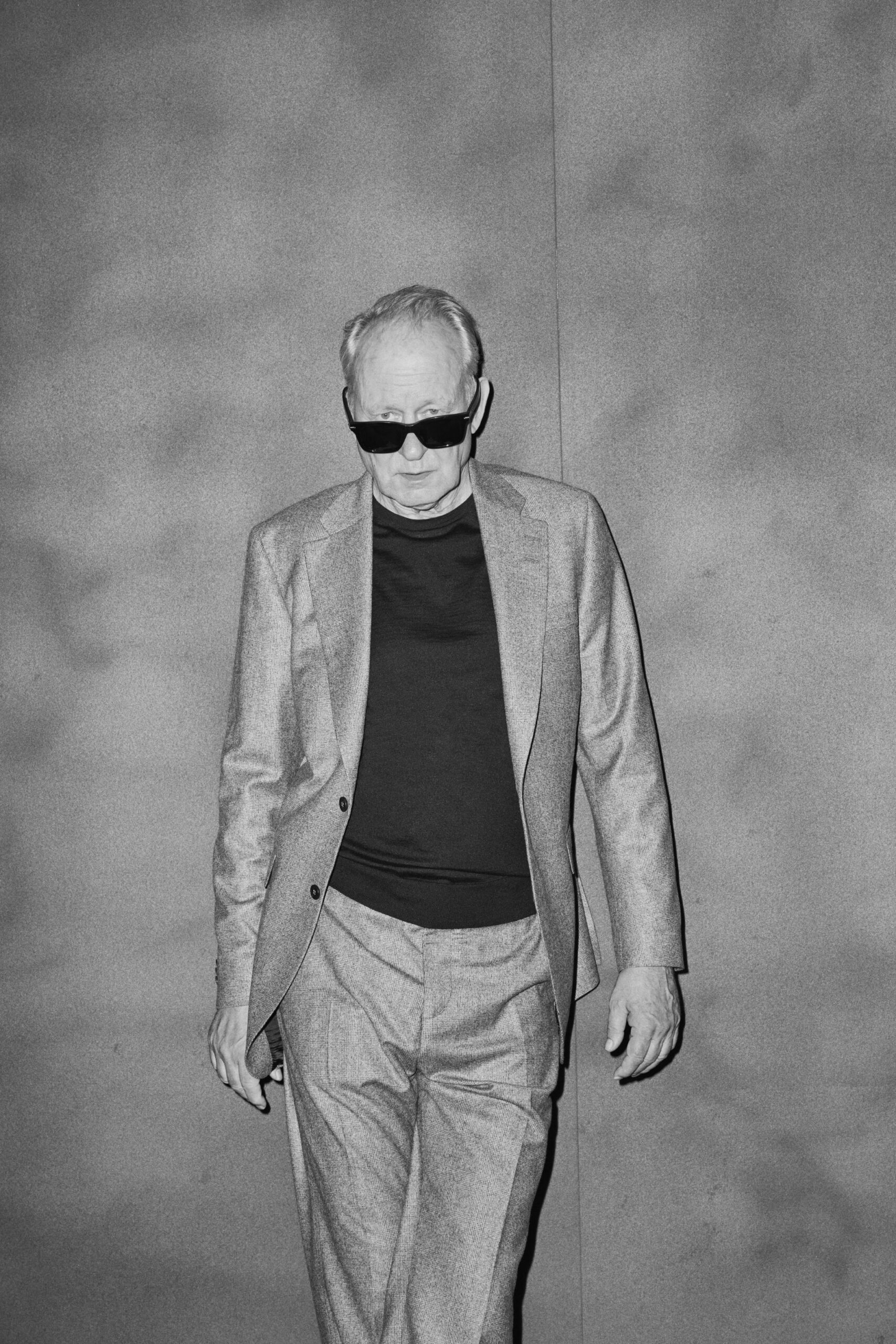 Portrait of Stellan Skarsgard by Jeremy Liebman wearing sunglasses and a suit against a gray background, interviewed by Robert Reich