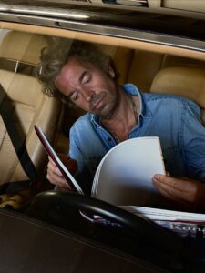 Friedrich Kunath reading, as seen through the hood of a car.