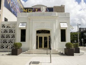 Patek Philippe's boutique in the Miami Design District, features a cream exterior, trimmed hedges, and light-informed windows