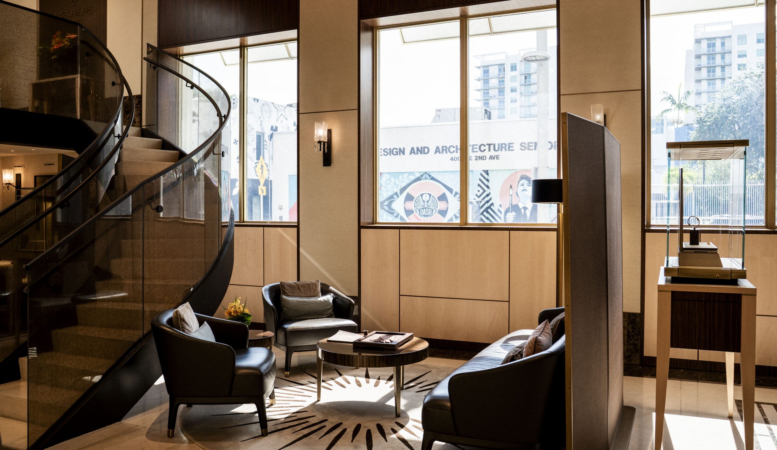 Patek Philippe's boutique in the Miami Design District, features a cream exterior, trimmed hedges, and light-informed windows