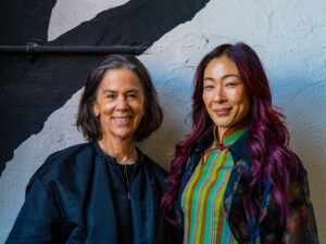 MoMA PS1 director Connie Butler and collector Sonya Yu pose in front of a painted wall.