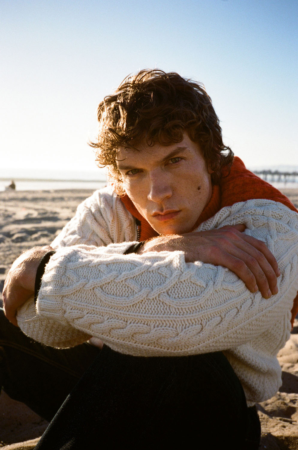 Actor Connor Storrie wears a cardigan and jeans by Dior at the beach.
