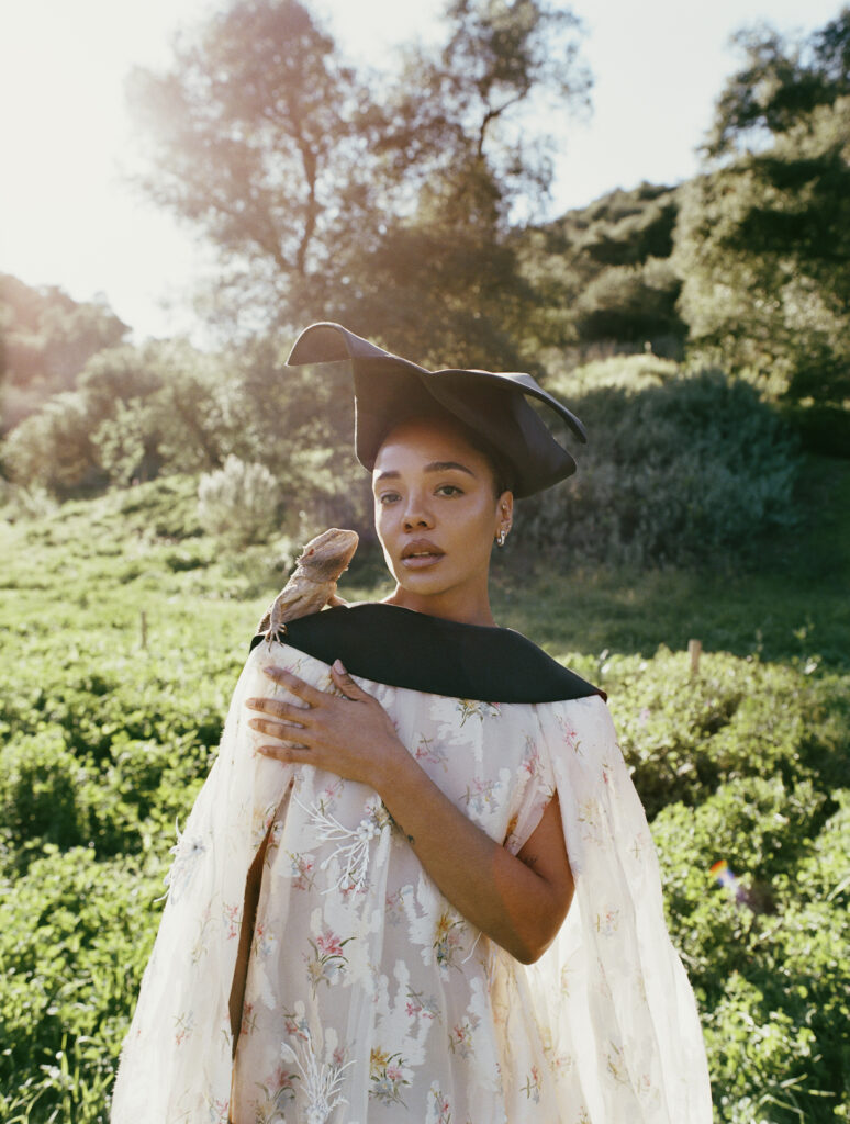 Actress Tessa Thompson poses in a grassy field with a lizard on her shoulder.