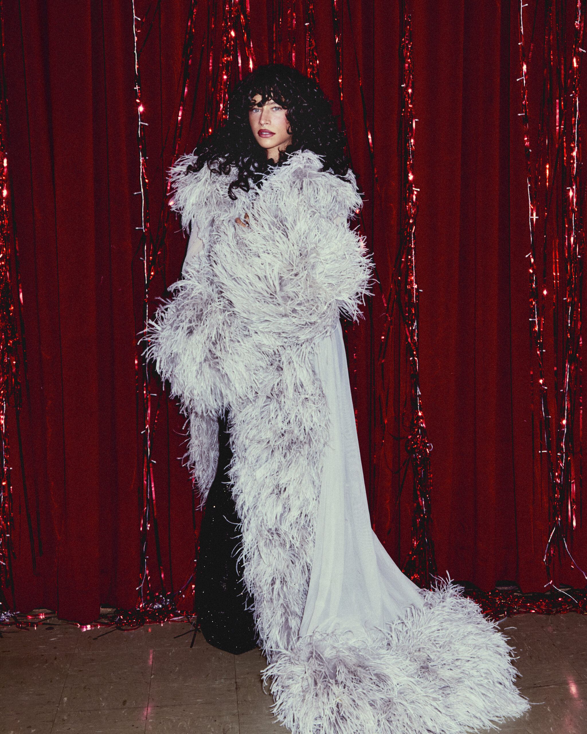 Actress Odessa A'zion poses in front of a red curtain in a blue fur coat by Gucci.