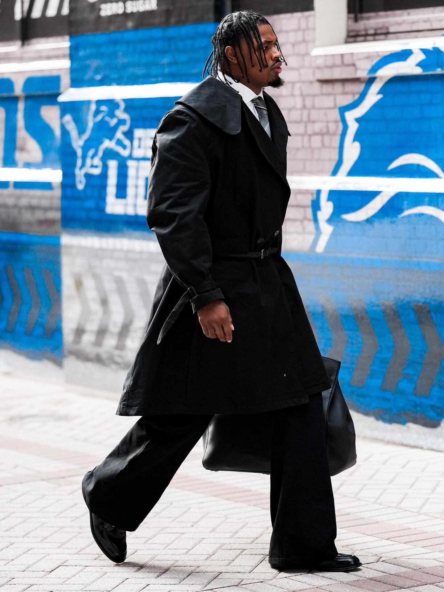 Al-Quadin Muhammed of the Detroit Lions in a black trench coat, white button-down, silver tie, leather bag, and black shoes