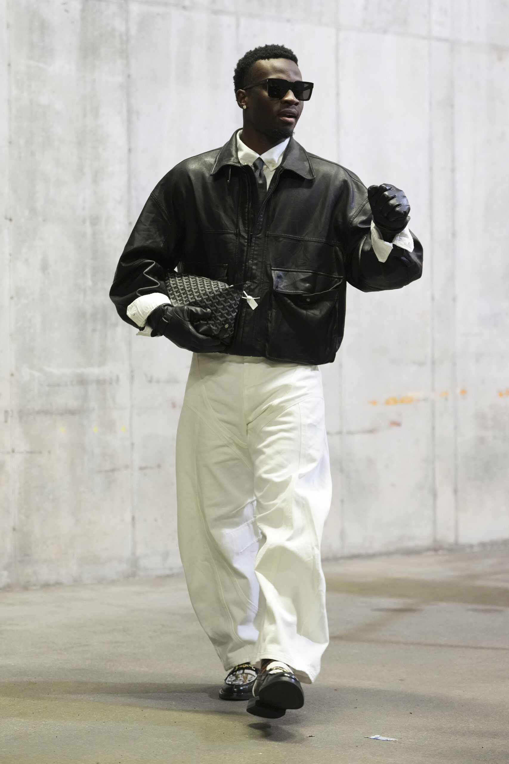 Mike Sainristil of the Washington Commanders in a leather jacket and gloves, sunglasses, black tie, white button-down, white slacks, and black sneakers in his tunnel look