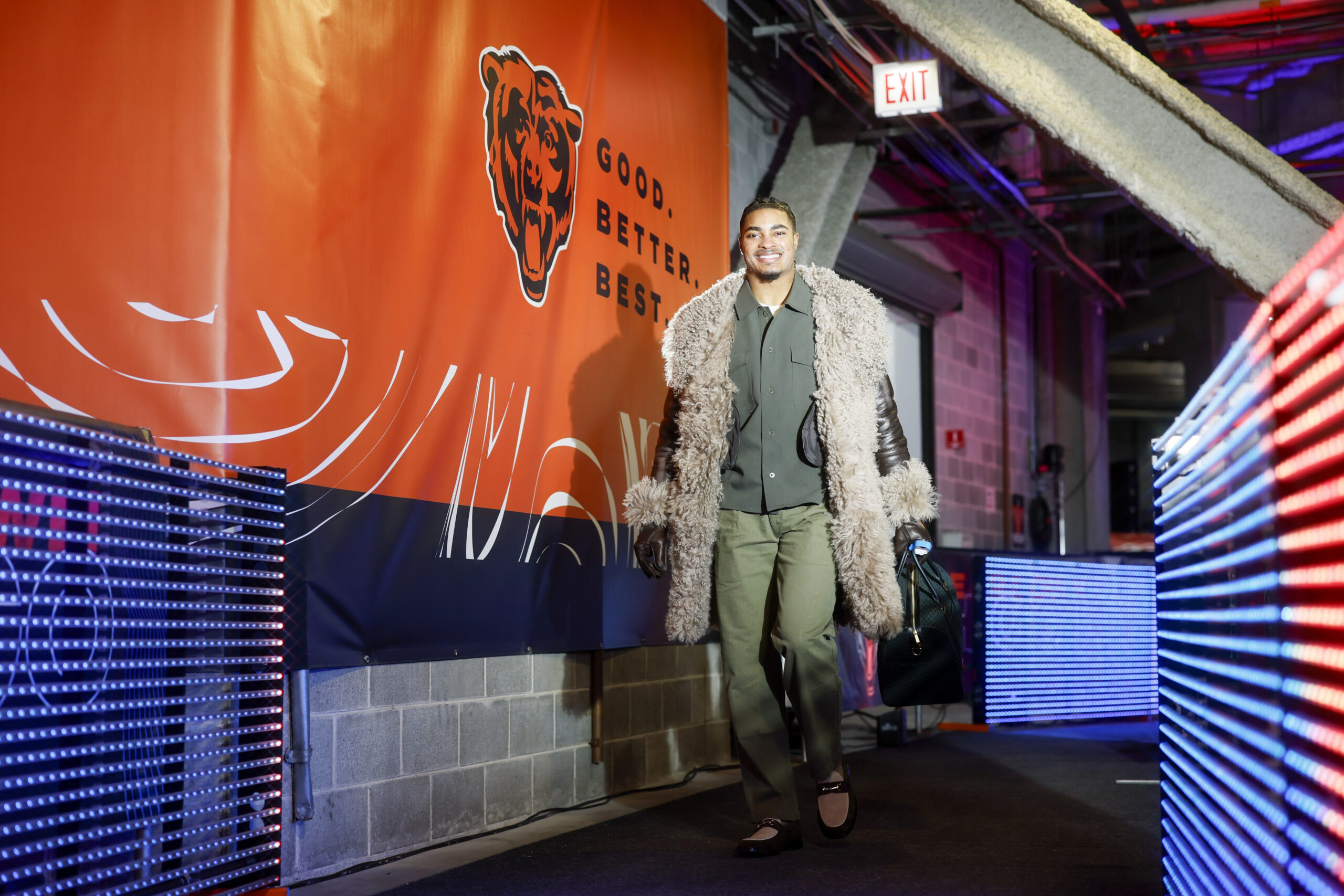 Jaquan Brisker of the Chicago Bears in a fur-lined coat, green button-down, green slacks, and brown shoes in the tunnel
