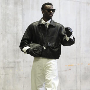 Mike Sainristil of the Washington Commanders in a leather jacket and gloves, sunglasses, black tie, white button-down, white slacks, and black sneakers in his tunnel look