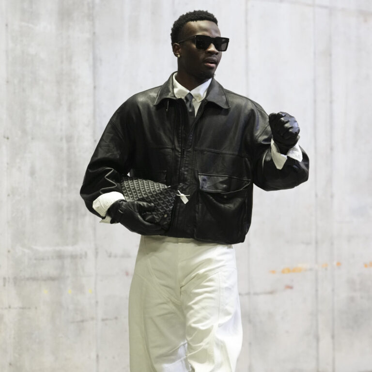 Mike Sainristil of the Washington Commanders in a leather jacket and gloves, sunglasses, black tie, white button-down, white slacks, and black sneakers in his tunnel look