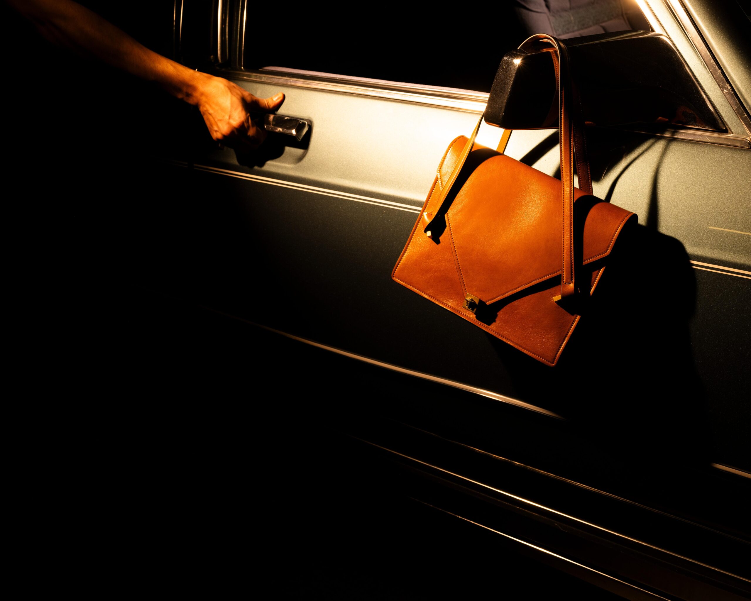 versace-ss26-campaign-tania-franco-klein A hand pulls on a car door as a brown bag hangs over the mirror in Versace's Spring/Summer 2026 campaign shot by Tania Franco Klein