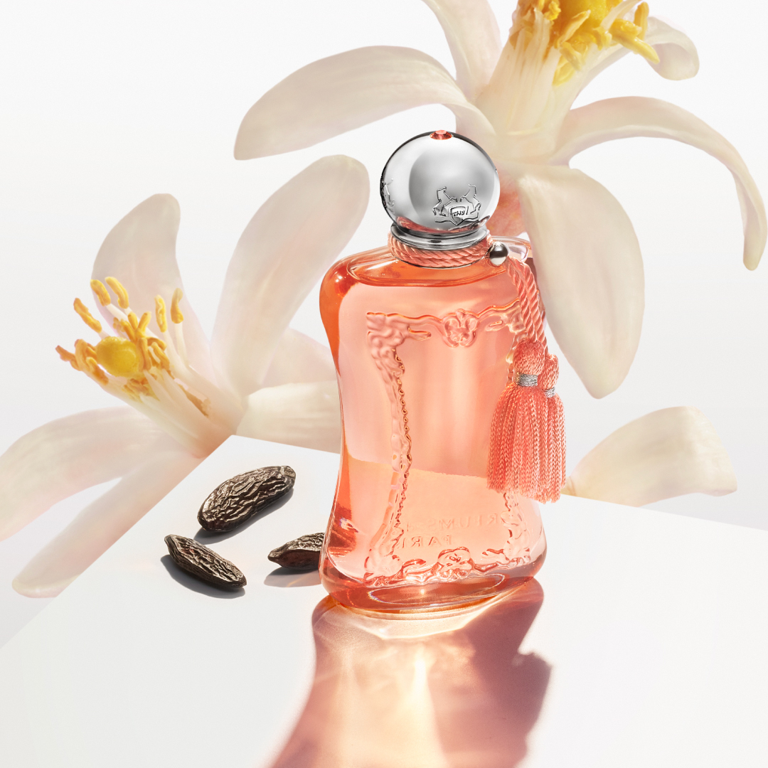 A model holds a bottle of Athénaïs fragrance wearing an orange dress