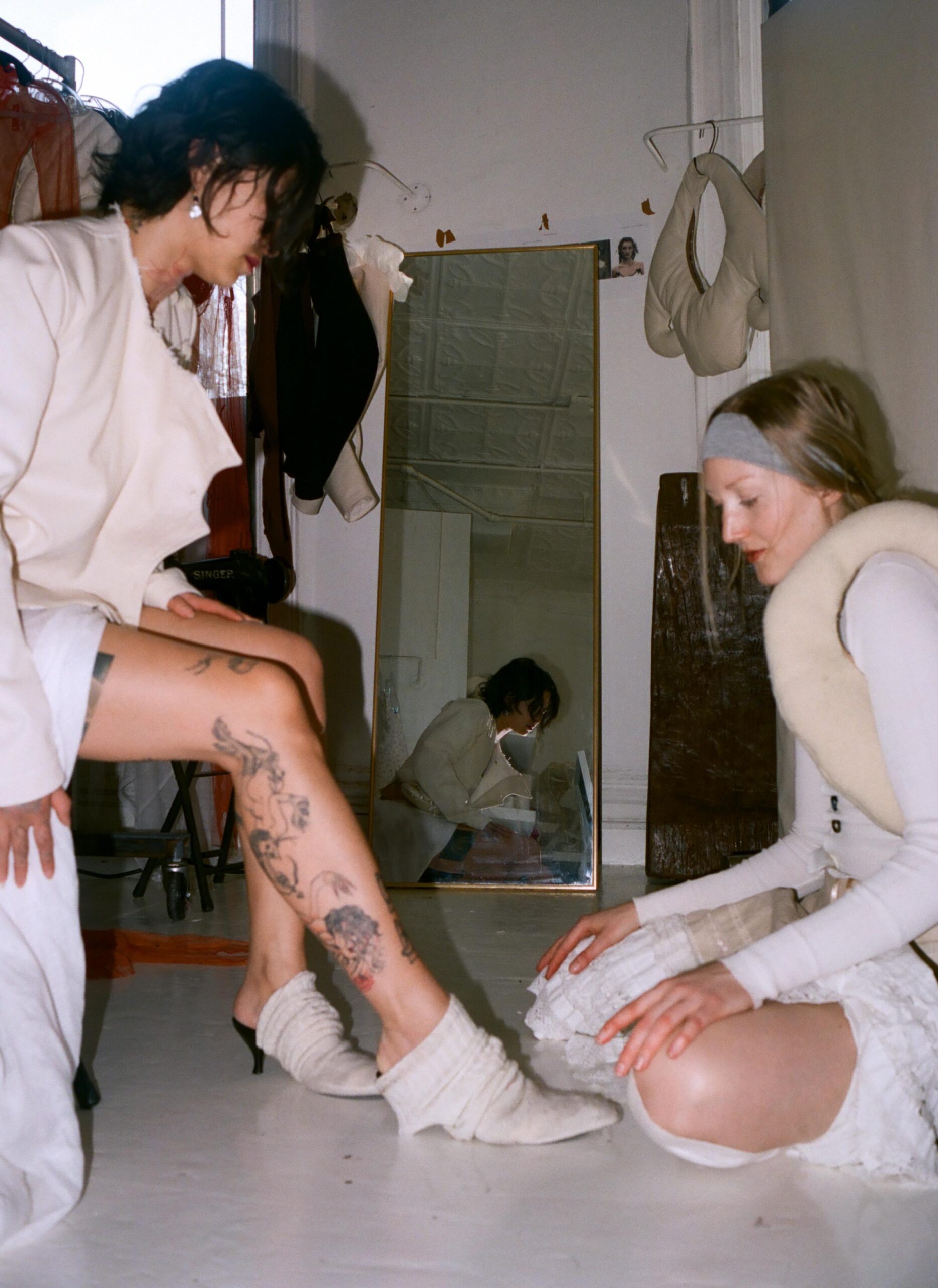 Zoe Gustavia Anna Whalen dresses Cato Young in her garments in a white-washed studio with a mirror behind them