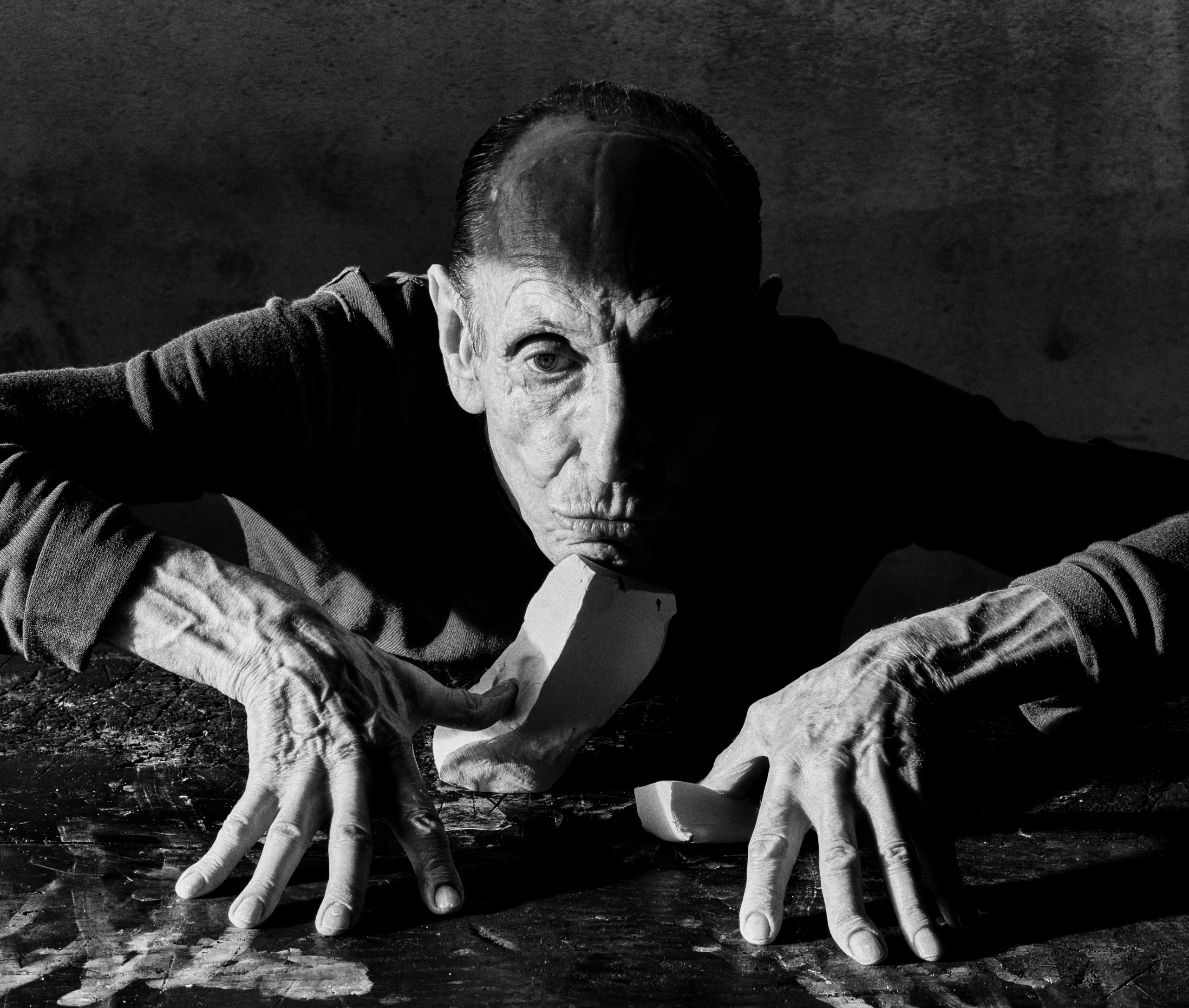 An older man in front of a block of clay in a photograph by Jack Davison